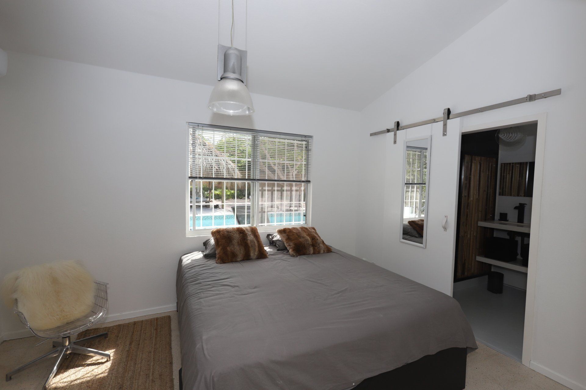 Slaapkamer met bed, schuifdeur, raam met uitzicht en hanglamp.
