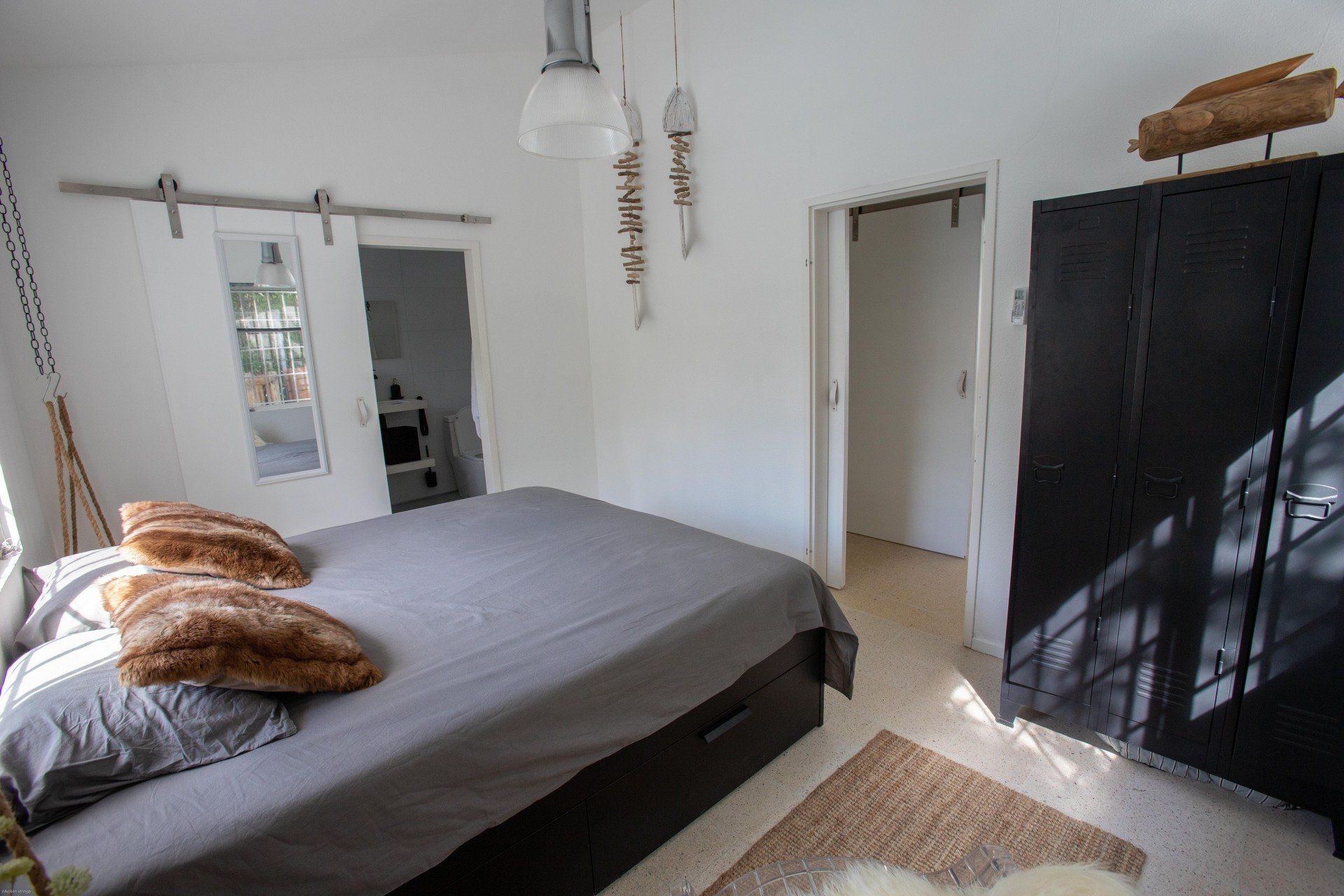 Slaapkamer met een bed, schuifdeuren en een zwarte kledingkast; zonlicht op de vloer.