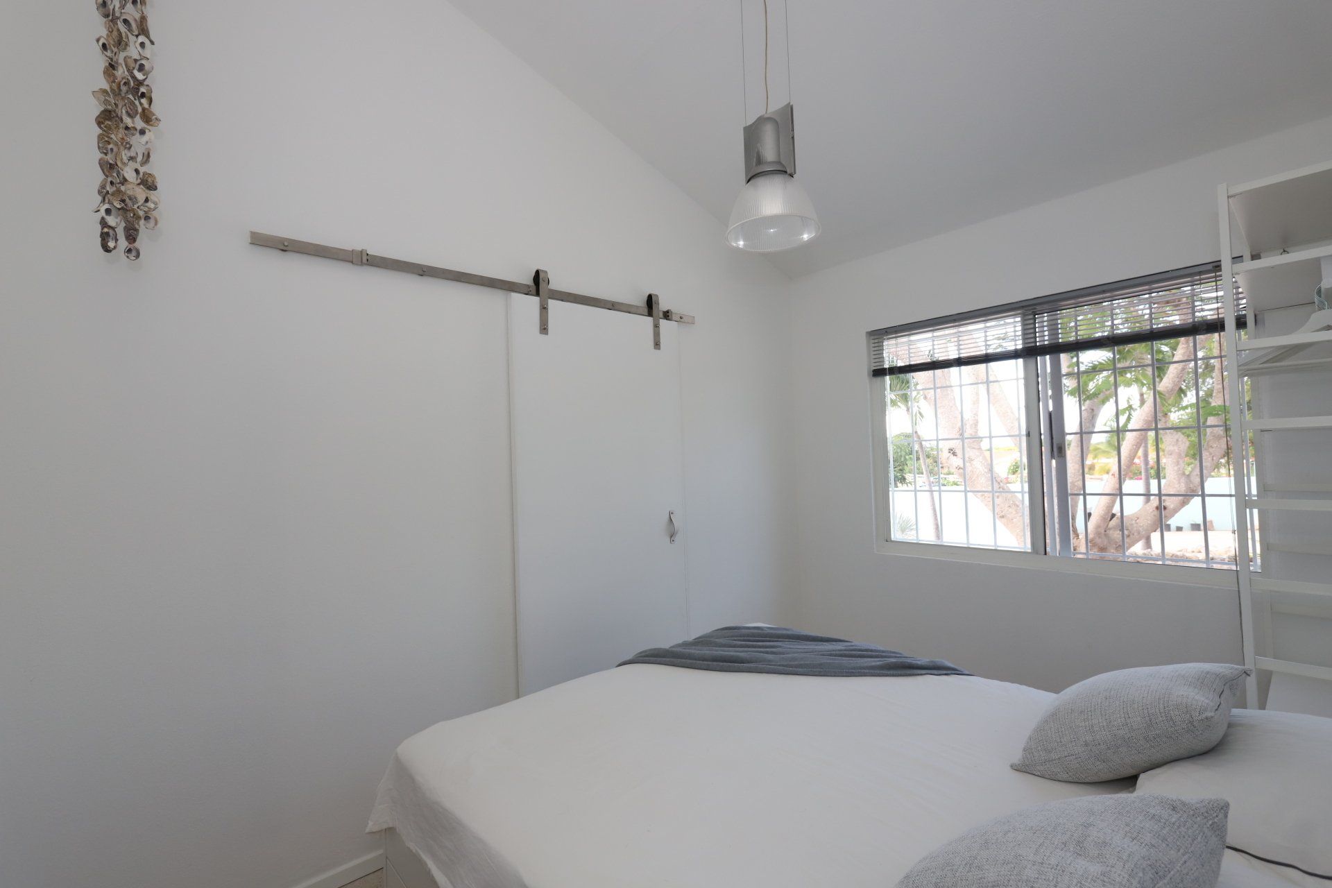 Slaapkamer met witte muren, schuifdeur, bed, raam en hanglamp.