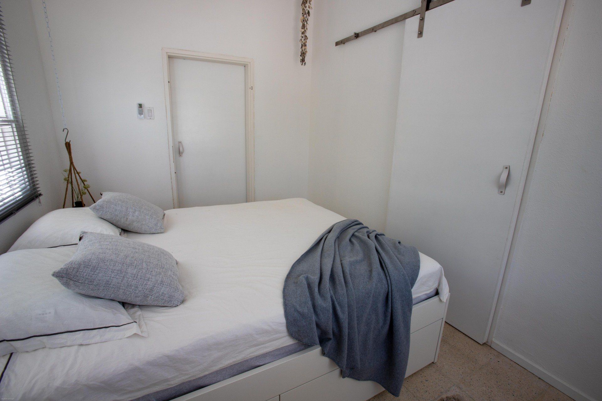 Witte slaapkamer met bed, kussens, grijze deken, deur en schuifdeur van de kledingkast.