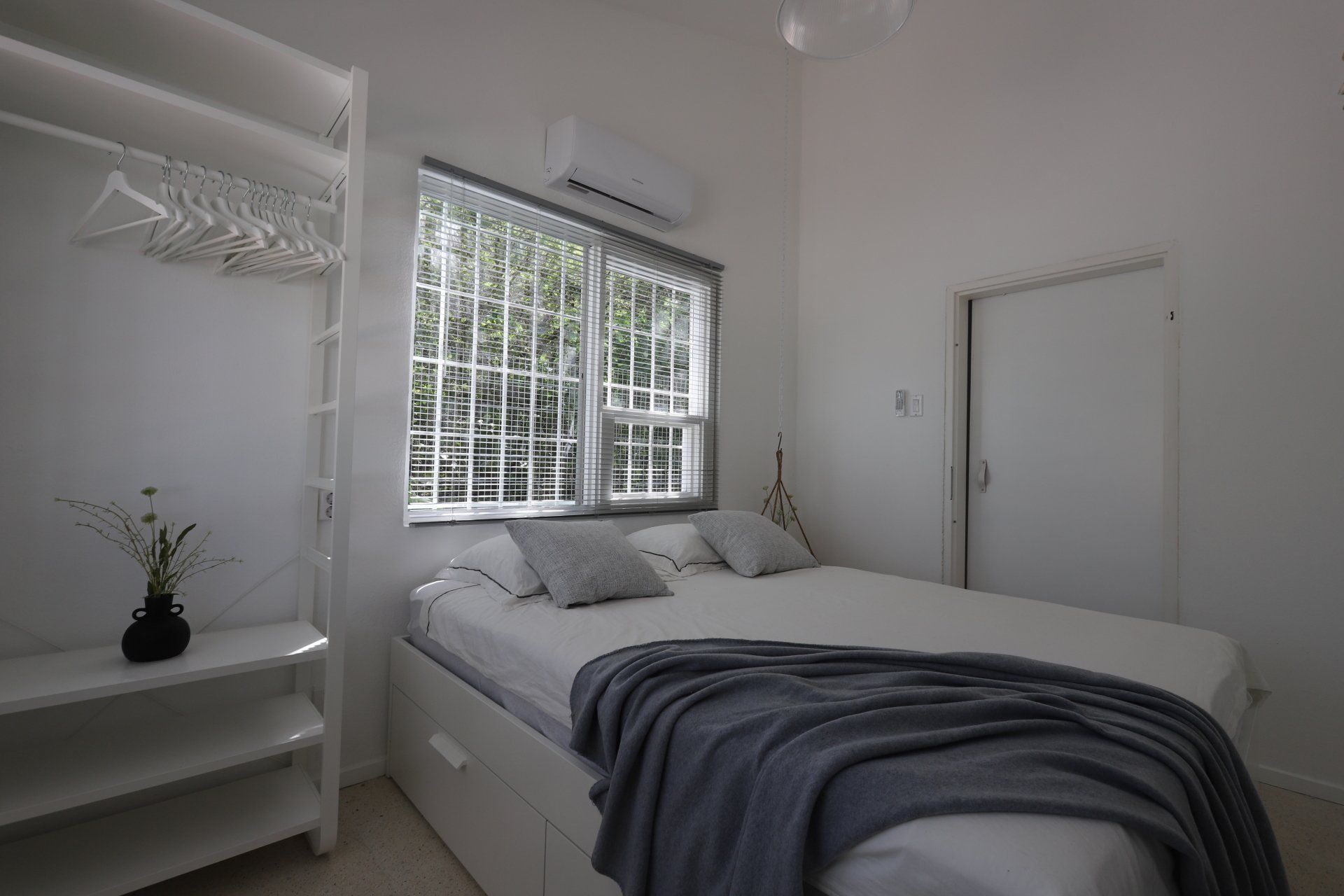 Slaapkamer met een bed, een raam met tralies, een witte kledingkast en een gesloten deur.