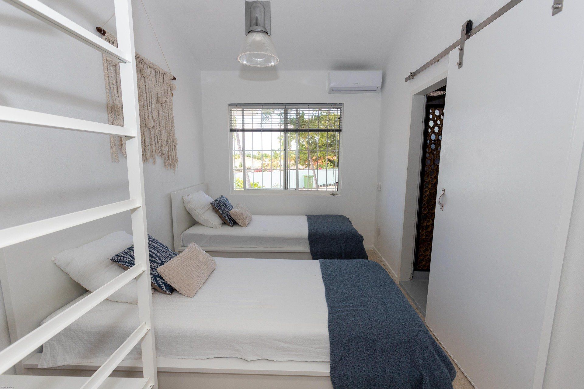 Witte slaapkamer met twee bedden, raam, decoratieve wanddecoratie en schuifdeur.