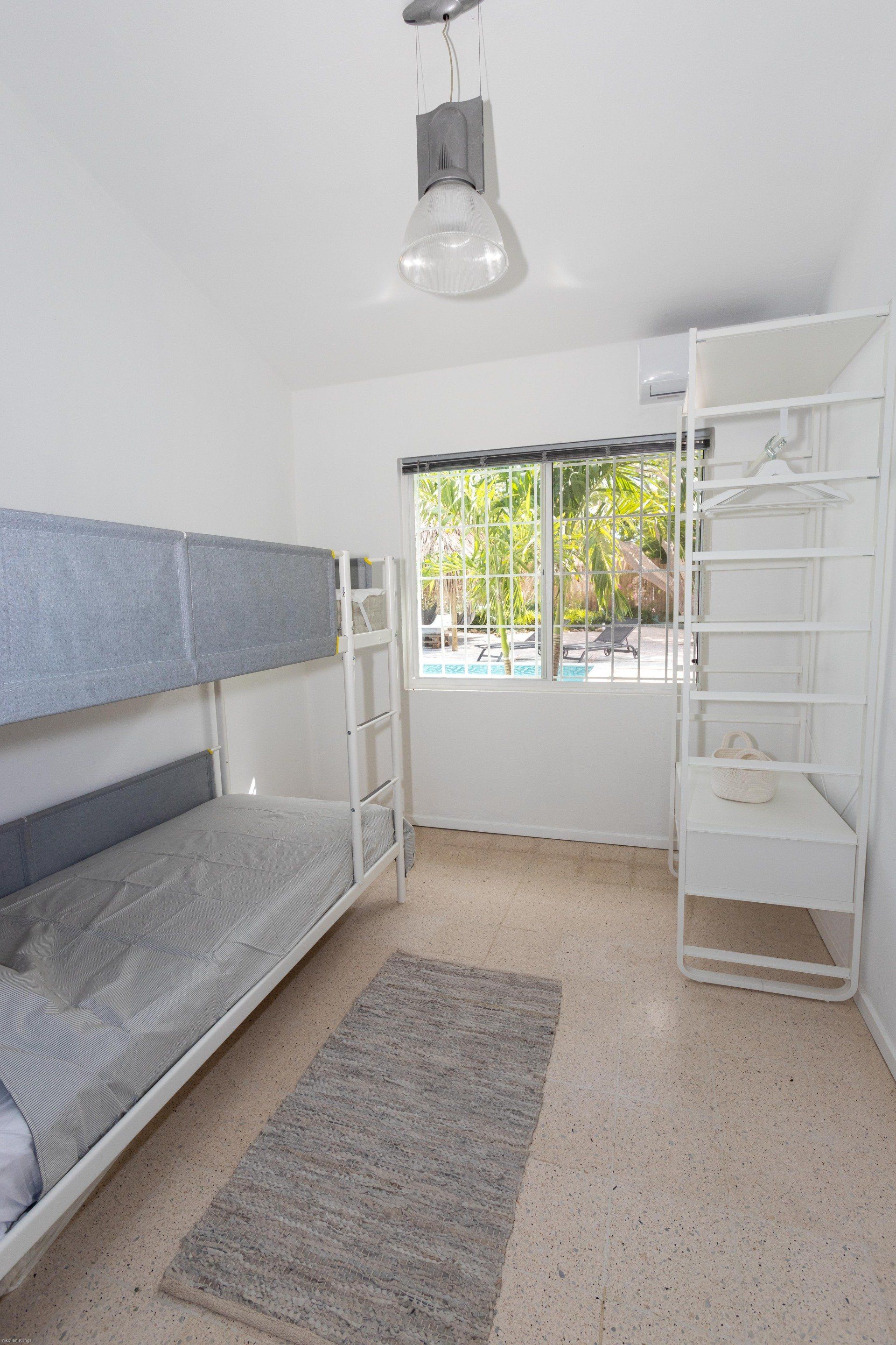 Witte slaapkamer met stapelbed, raam, open kast en grijs vloerkleed.
