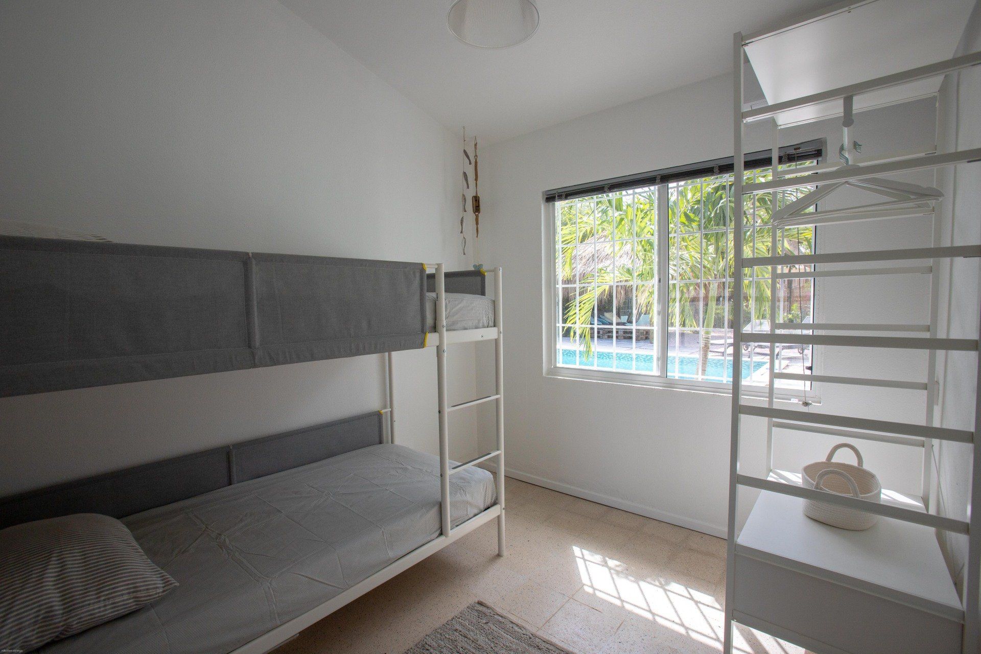 Stapelbedden in een witte slaapkamer met een raam dat uitkijkt op het zwembad.