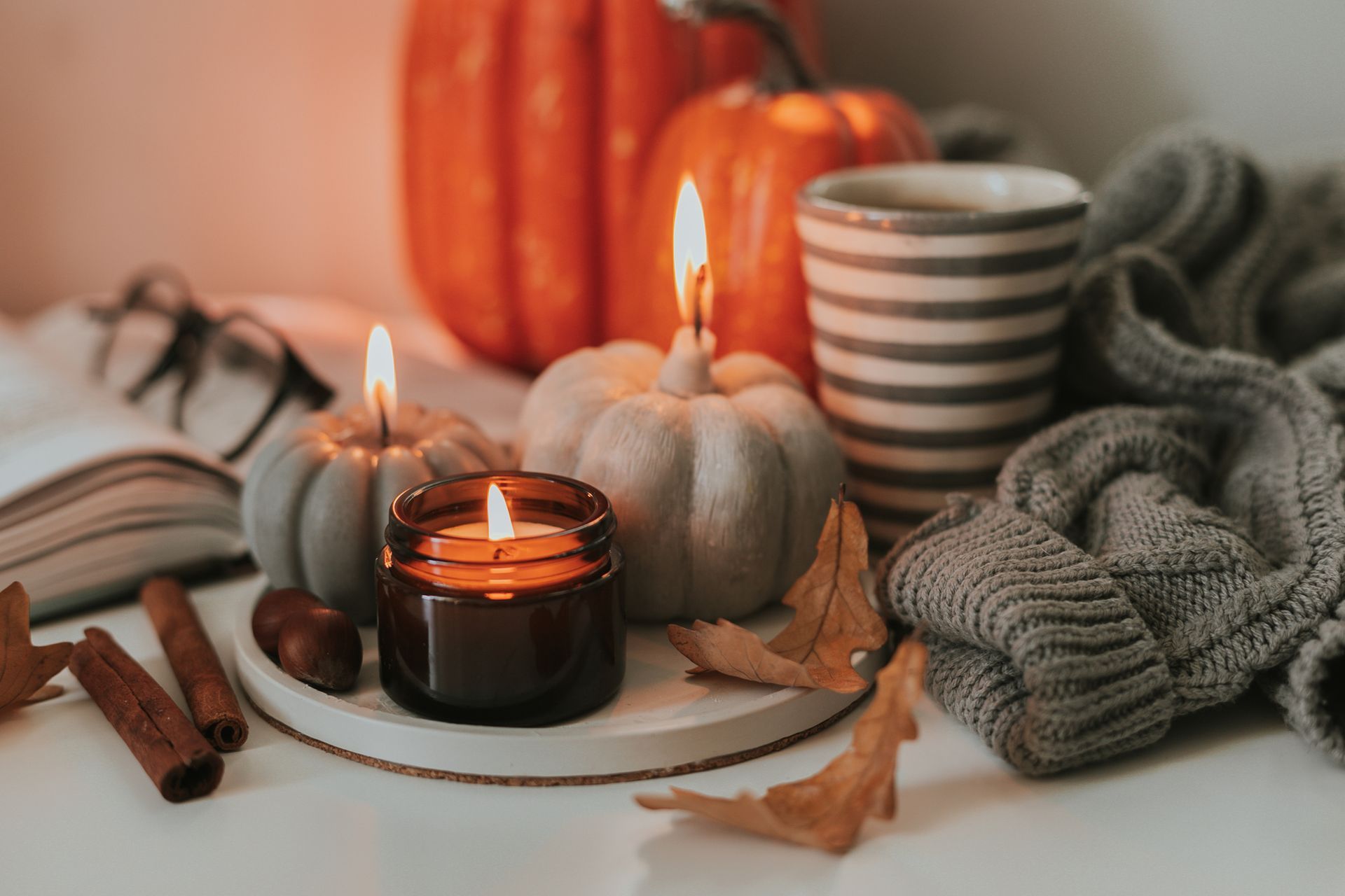 A table topped with candles, pumpkins, cinnamon sticks, a book and a cup of coffee.