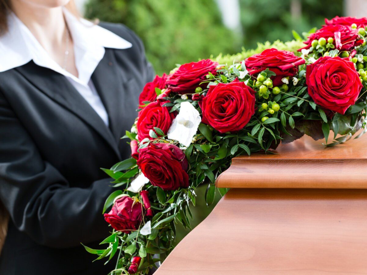 A woman is holding a wreath of red roses in front of a coffin.