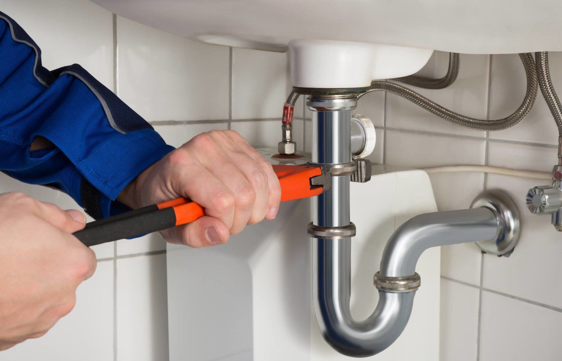 A plumber is fixing a sink pipe with a wrench.