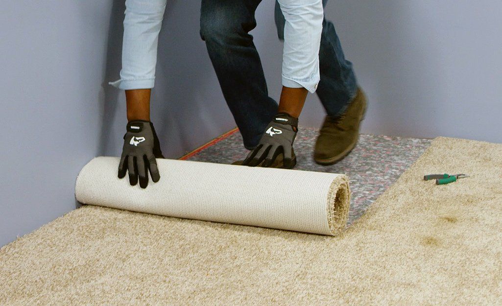 A person is rolling a roll of carpet on the floor.