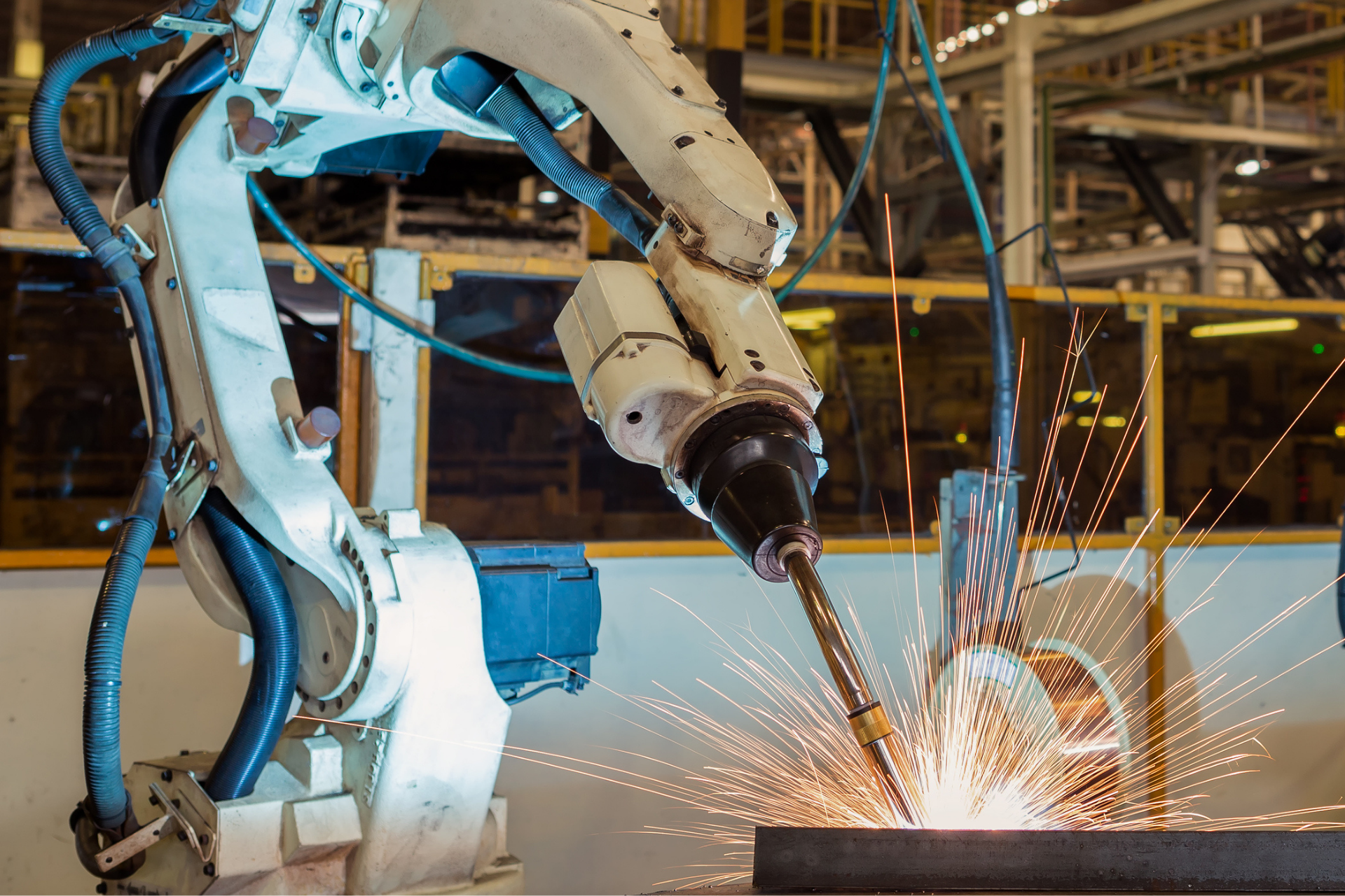 A robotic arm welds a metal piece in a factory, emitting bright sparks.