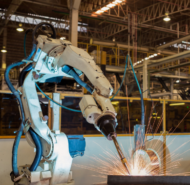 An industrial robotic arm welding metal in a factory, emitting bright sparks.