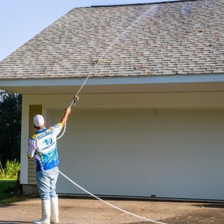 A man is cleaning the roof of a garage with a pressure washer.