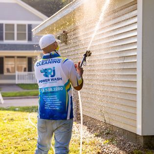 A man is cleaning the side of a house with a pressure washer.