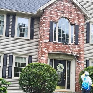 A man is cleaning the windows of a large brick house.