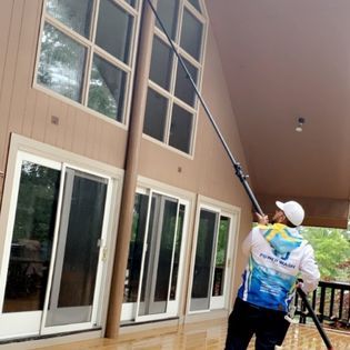 A man is cleaning the windows of a house with a high pressure washer.