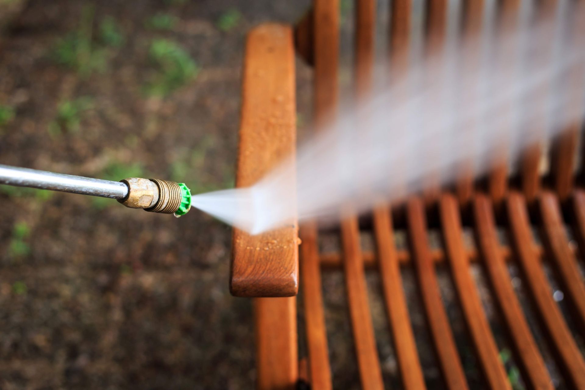 A person is cleaning a wooden chair with a high pressure washer.
