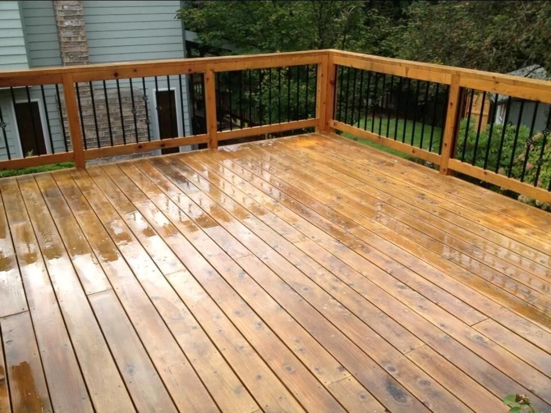 A wooden deck with a metal railing and a house in the background