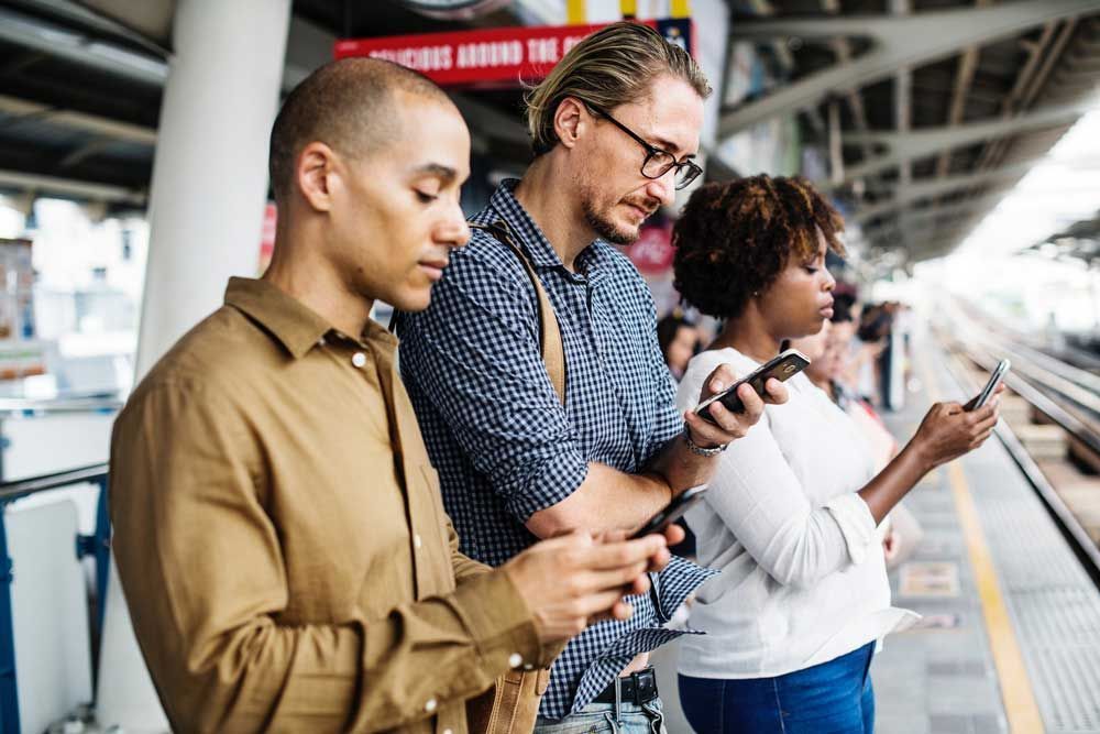A group of people are looking at their phones at a train station. A group of people are looking at their phones at a train station.