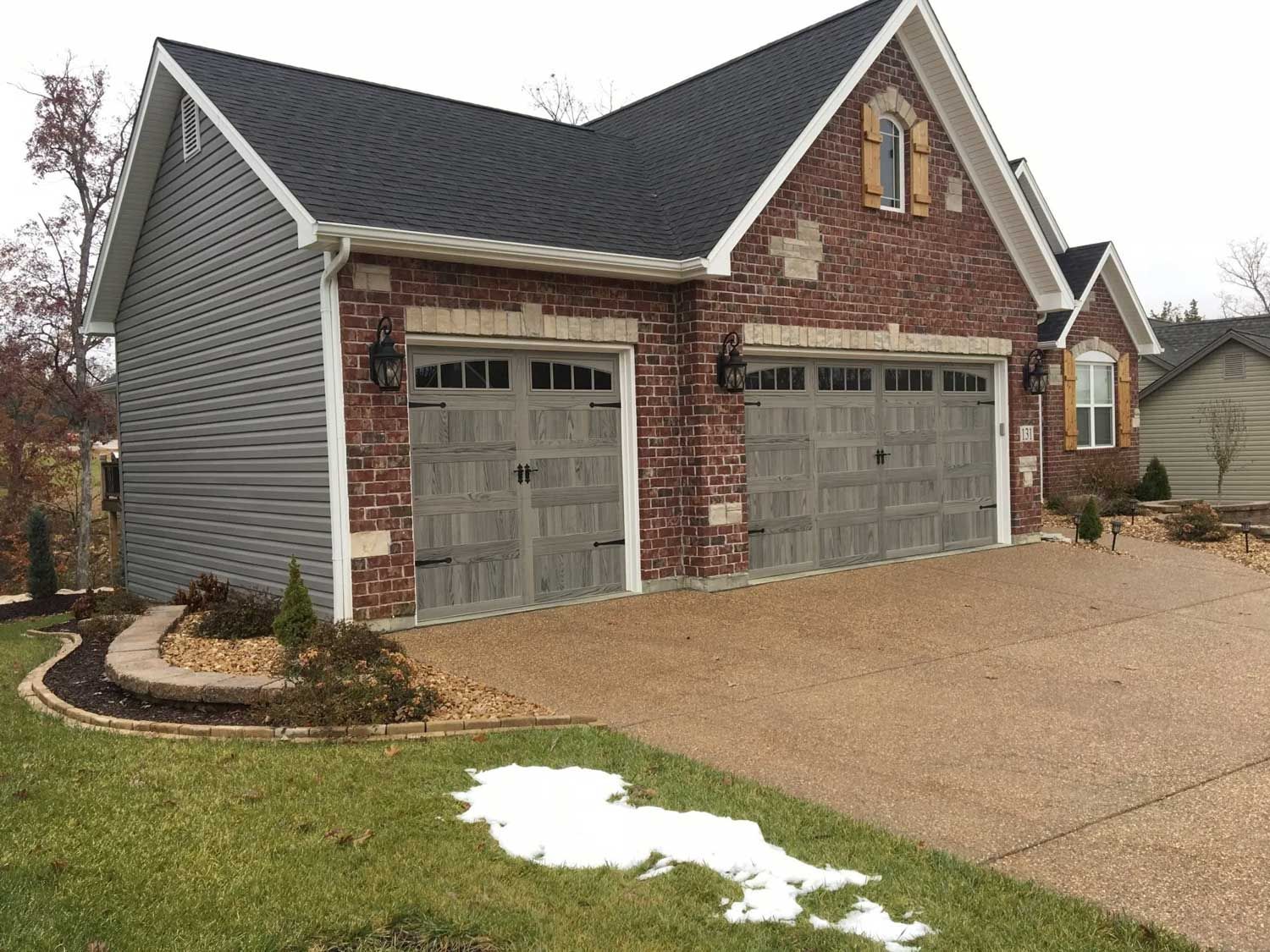 A large brick house with two garage doors and a driveway. A large brick house with two garage doors and a driveway.