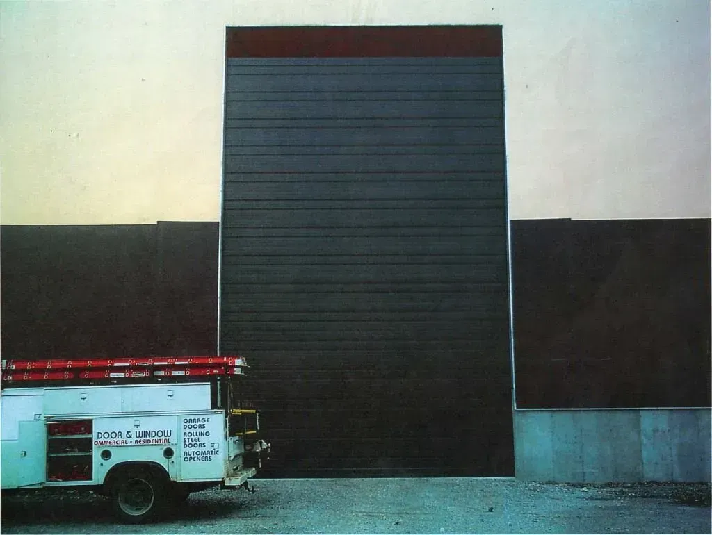 A white utility truck is parked in front of a large garage door