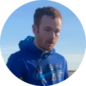 Man in blue hoodie, looking down, set against a bright sky.