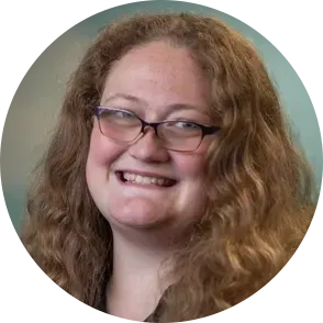 Woman with long, wavy brown hair and glasses smiles.