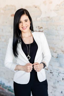 Smiling woman in a white blazer and black shirt, outside.