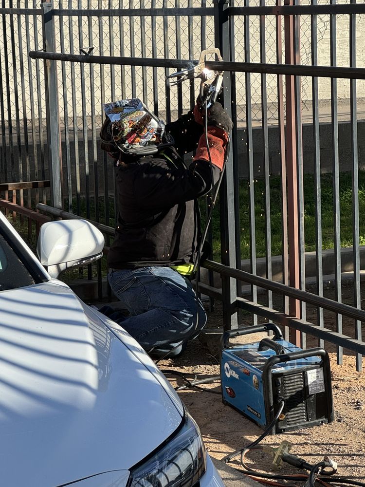 A man is welding a fence next to a car.