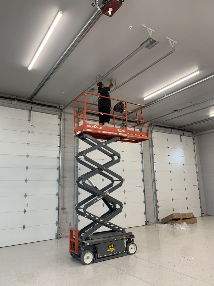 A man is standing on a scissor lift in a garage.
