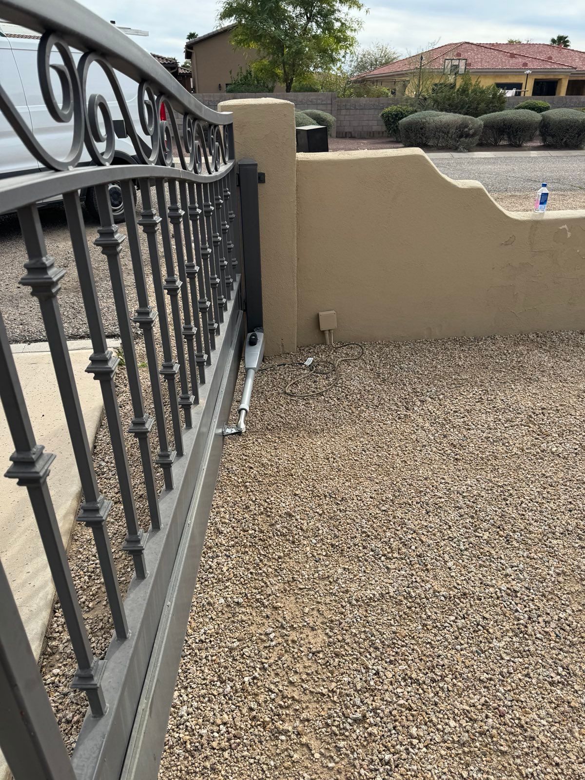 A sliding gate is sitting on top of a gravel driveway next to a wall.
