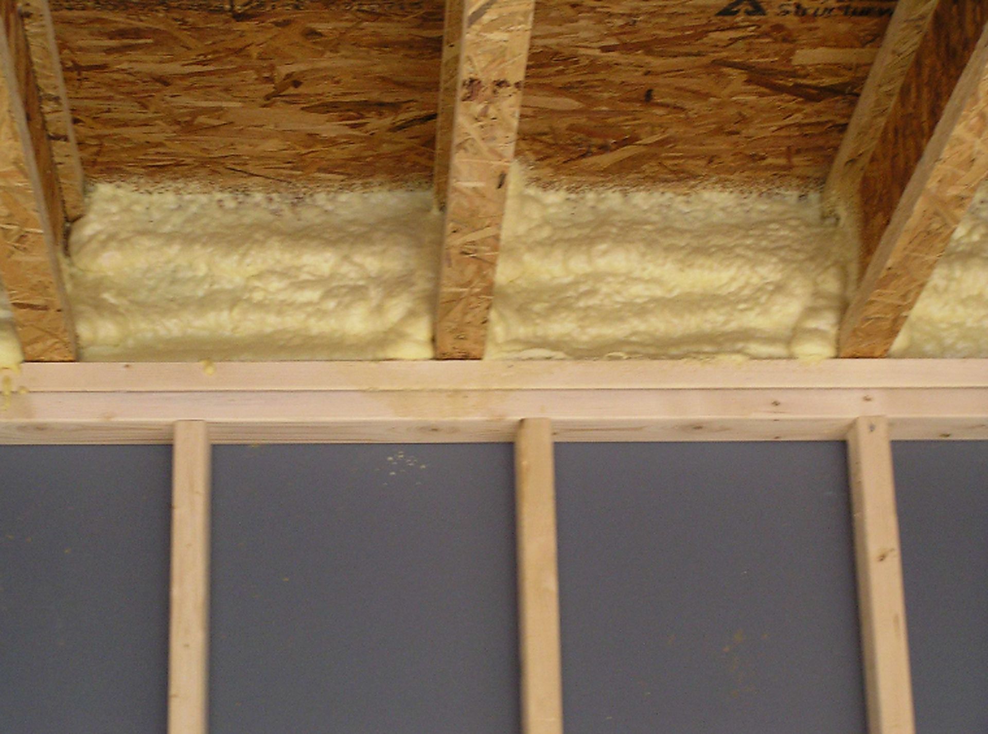Spray foam fills ceiling cavities between wood joists after Spray Foam Insulation Services in Muncie, IN were completed.