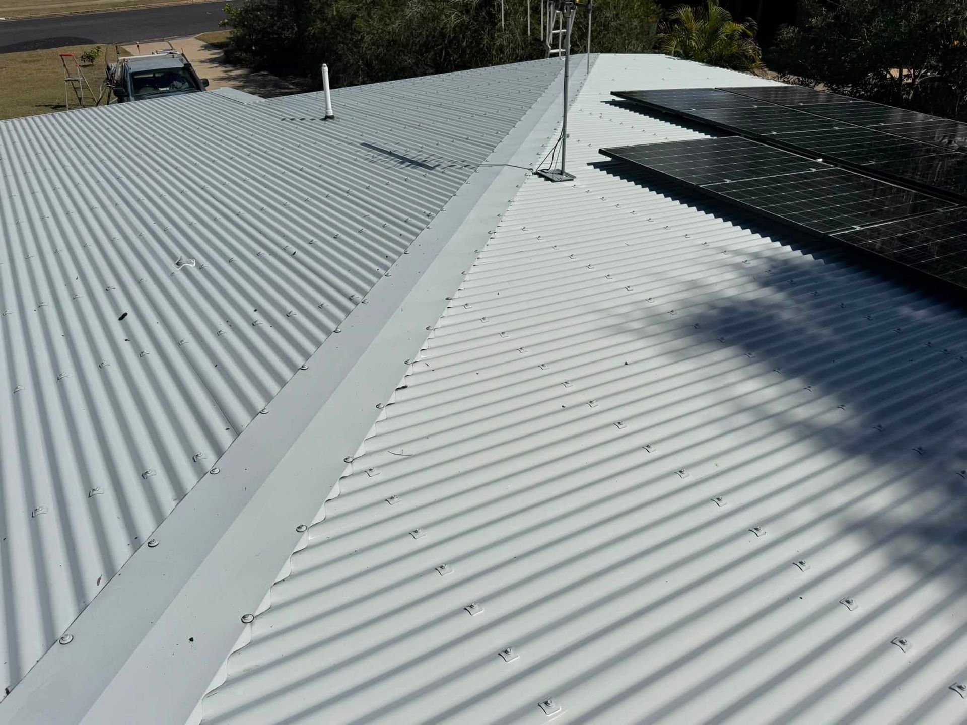 White Corrugated Metal Roof With a Central Seam and Dark Solar Panels on the Right Side — CPR Exterior Cleaning in Bundaberg North, QLD