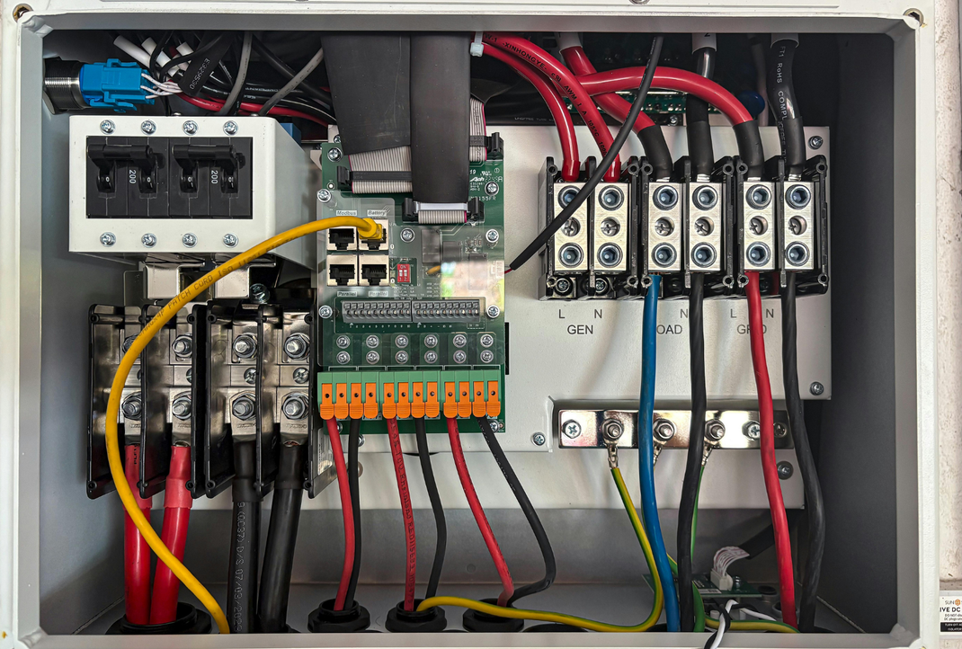 An open gray electrical junction box featuring wiring, terminal blocks, a circuit breaker, and a central circuit board.