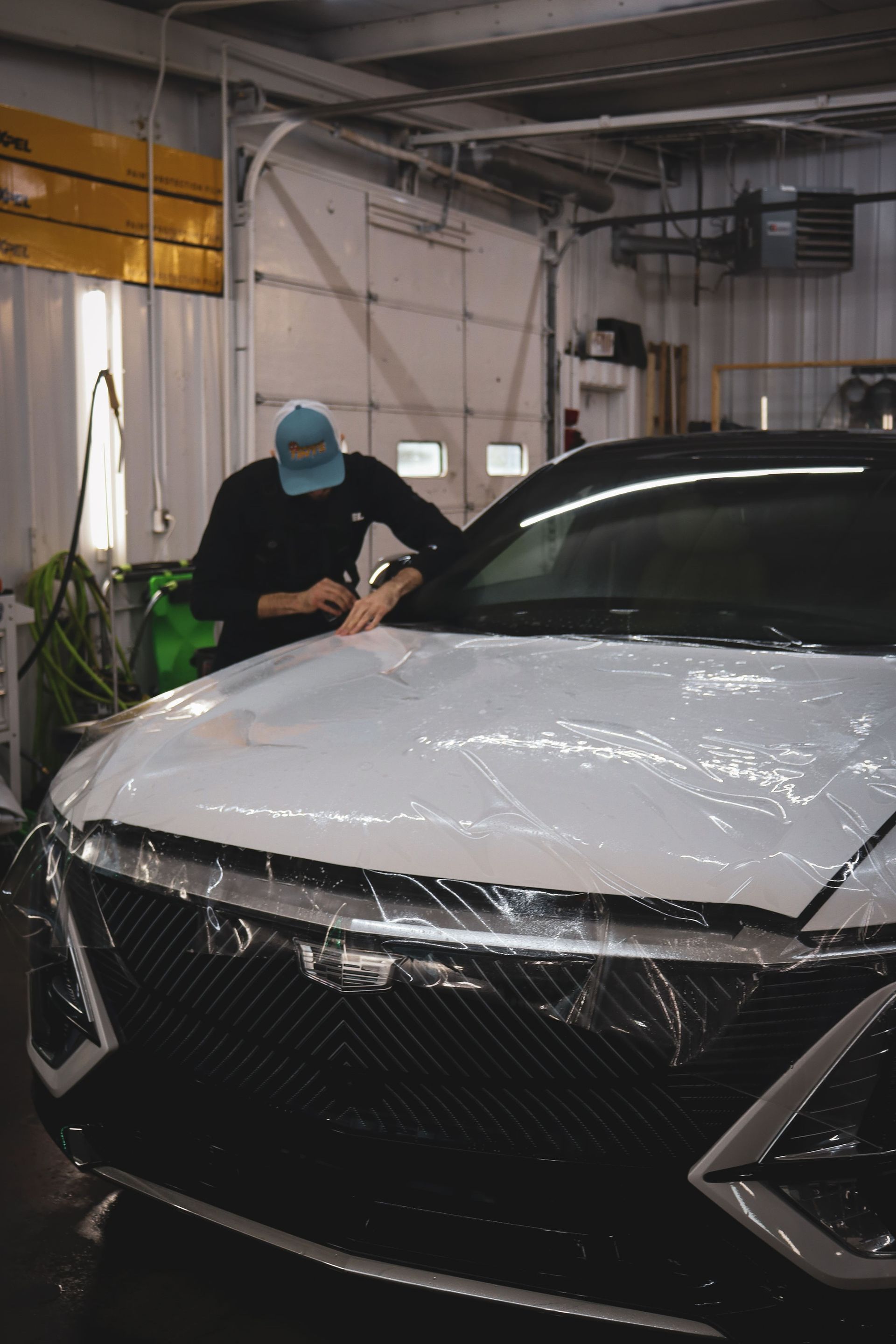 A man is wrapping a white car in plastic in a garage.