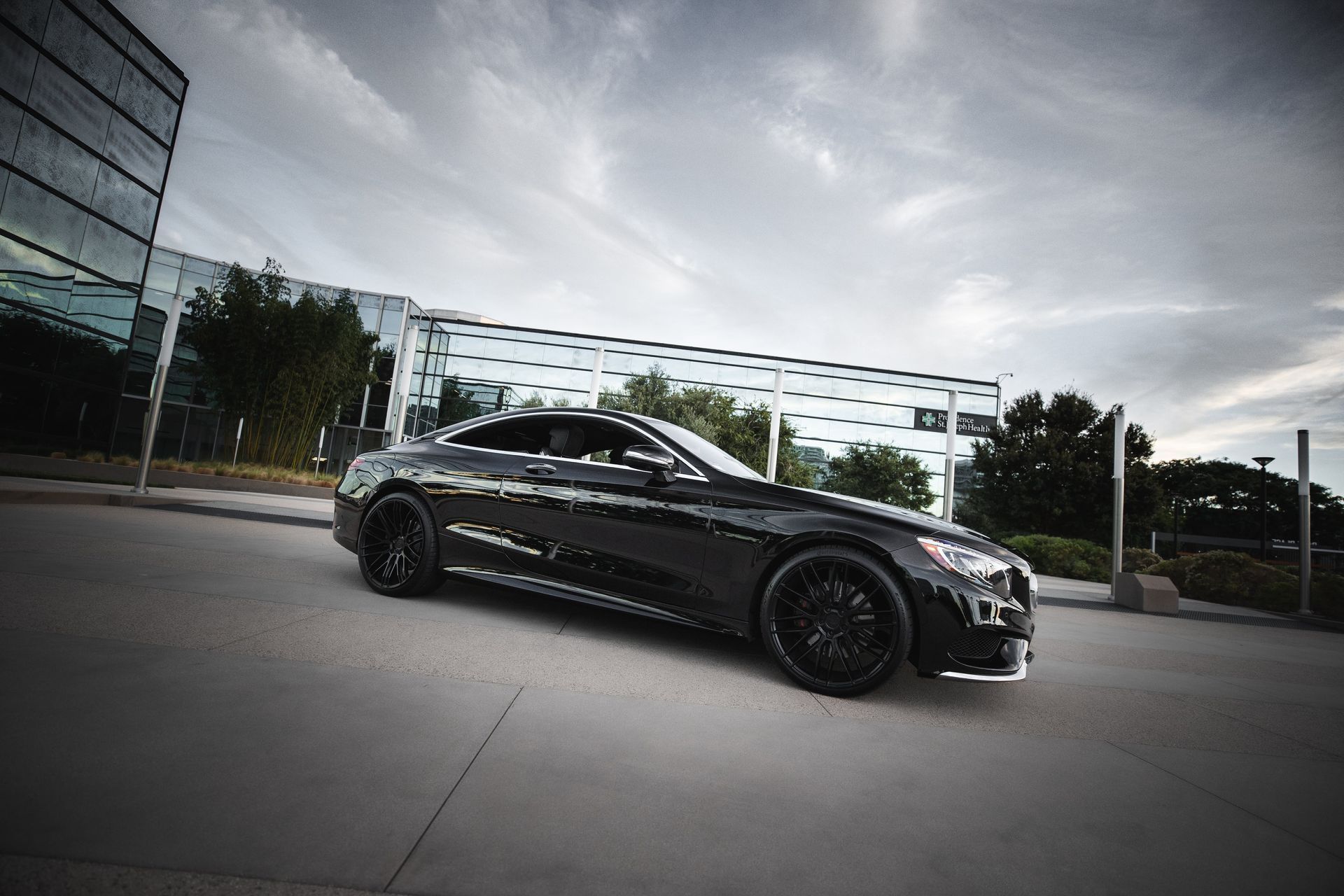 A black car is parked on the side of the road in front of a building.