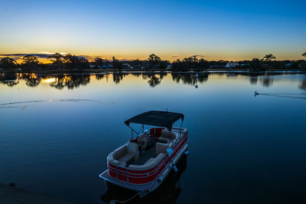 A Pontoon Boat Is Floating on A Lake at Sunset — TJL Business Advisors & Accountants in Forster, NSW