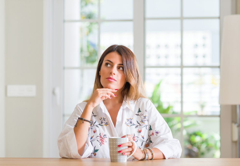A Woman is Sitting at a Table Holding a Cup of Coffee and Looking Up — TJL Business Advisors & Accountants in Forster, NSW