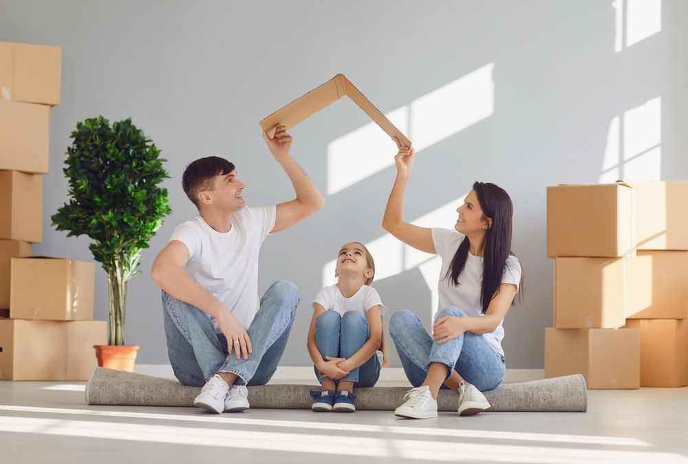 A Family is Sitting on the Floor in Their New Home Holding a Cardboard House — TJL Business Advisors & Accountants in Forster, NSW