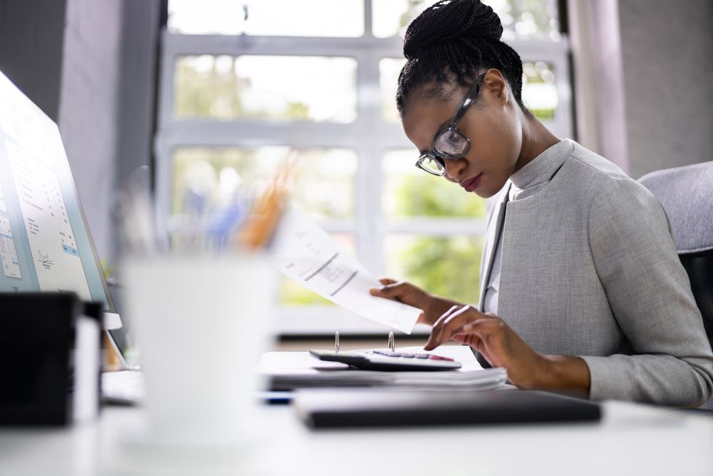 A Woman is Sitting at a Desk With a Calculator and a Piece of Paper — TJL Business Advisors & Accountants in Taree, NSW