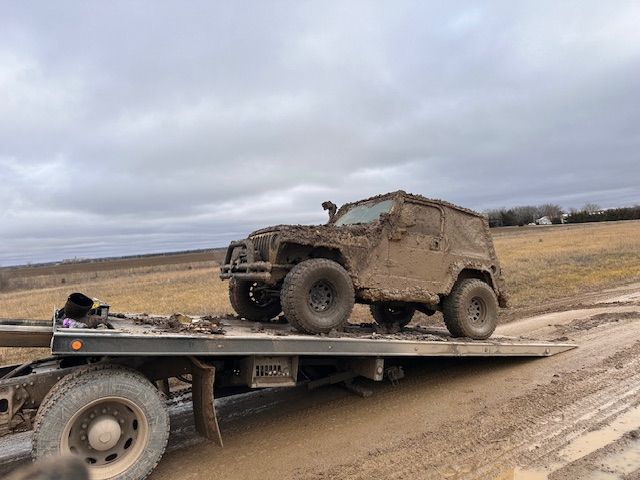 A muddy jeep is sitting on top of a flatbed tow truck.