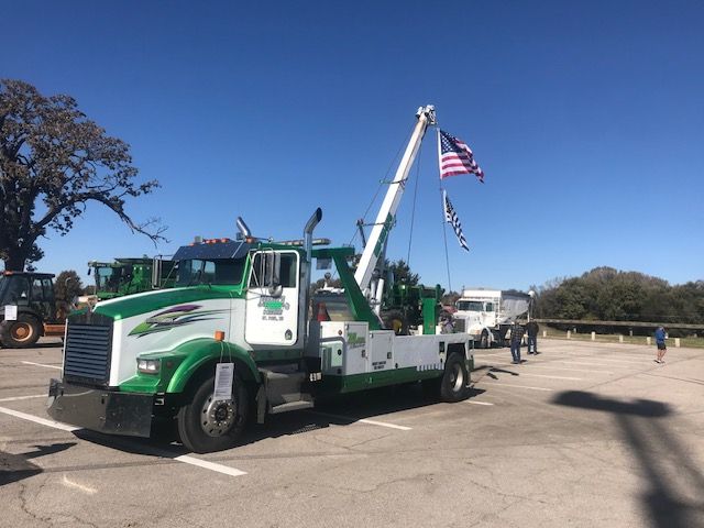 A green and white tow truck is parked in a parking lot.