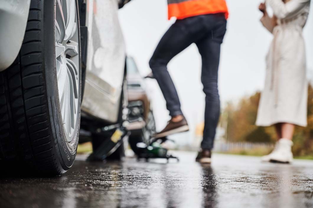 A man is changing a tire on a car in the rain.