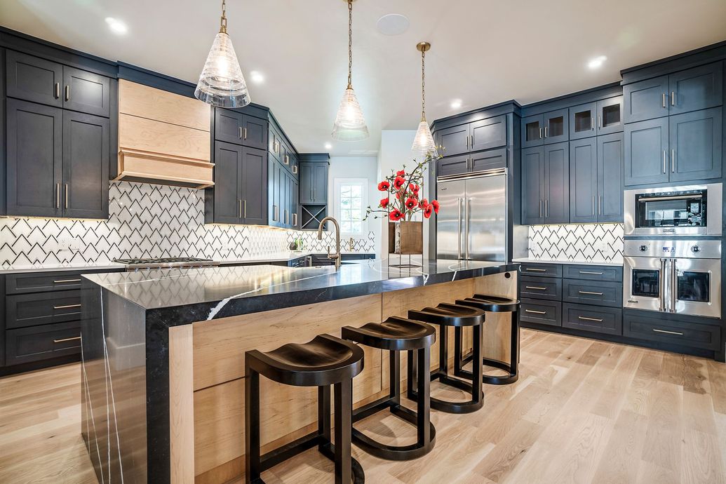 Modern kitchen with dark cabinets, marble island, pendant lights, and four black stools