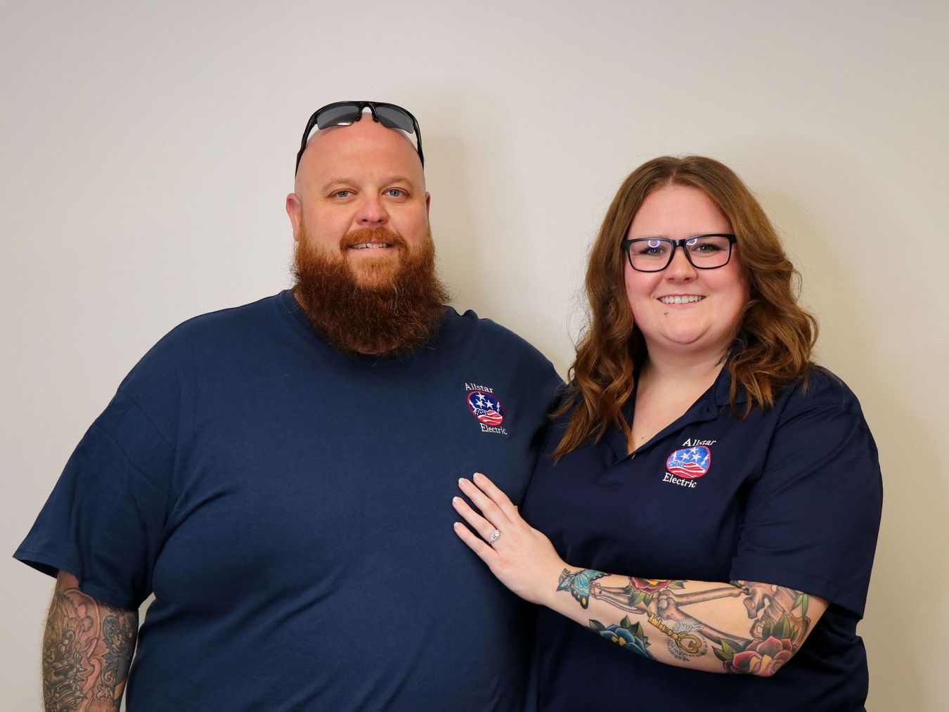Three people standing side by side against a plain wall, wearing matching navy shirts and smiling.