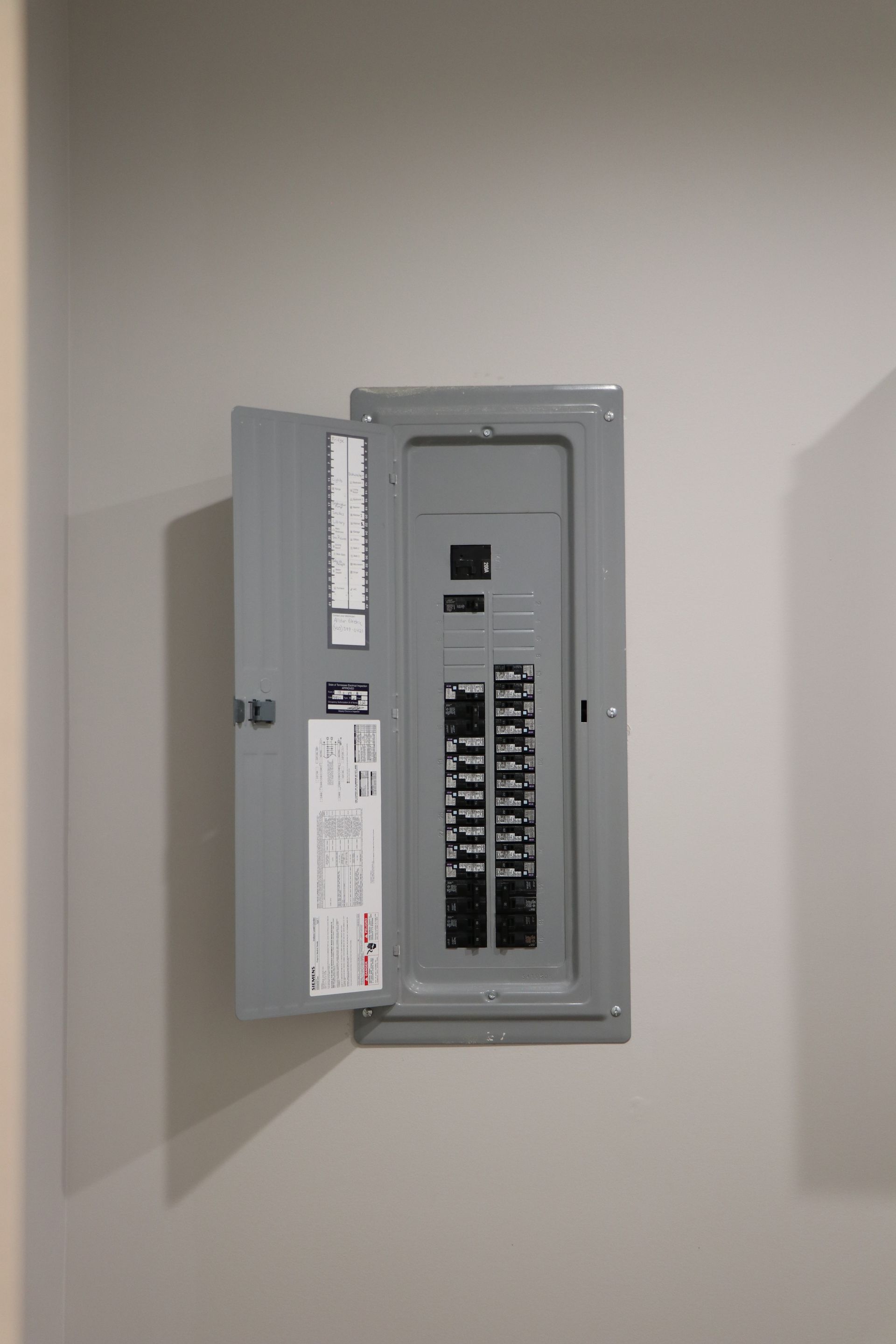 Allstar Electrical Cleveland, Tennessee Open electrical breaker panel on a beige wall, with rows of switches visible