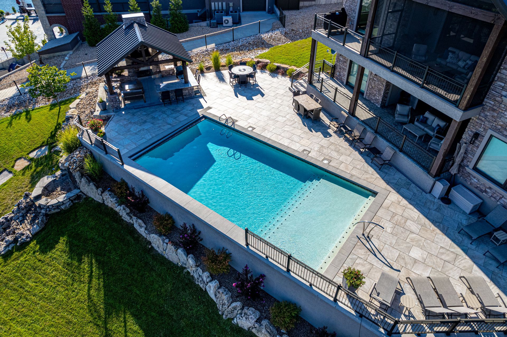 Aerial view of a turquoise swimming pool beside a modern house with lounge chairs and a patio.