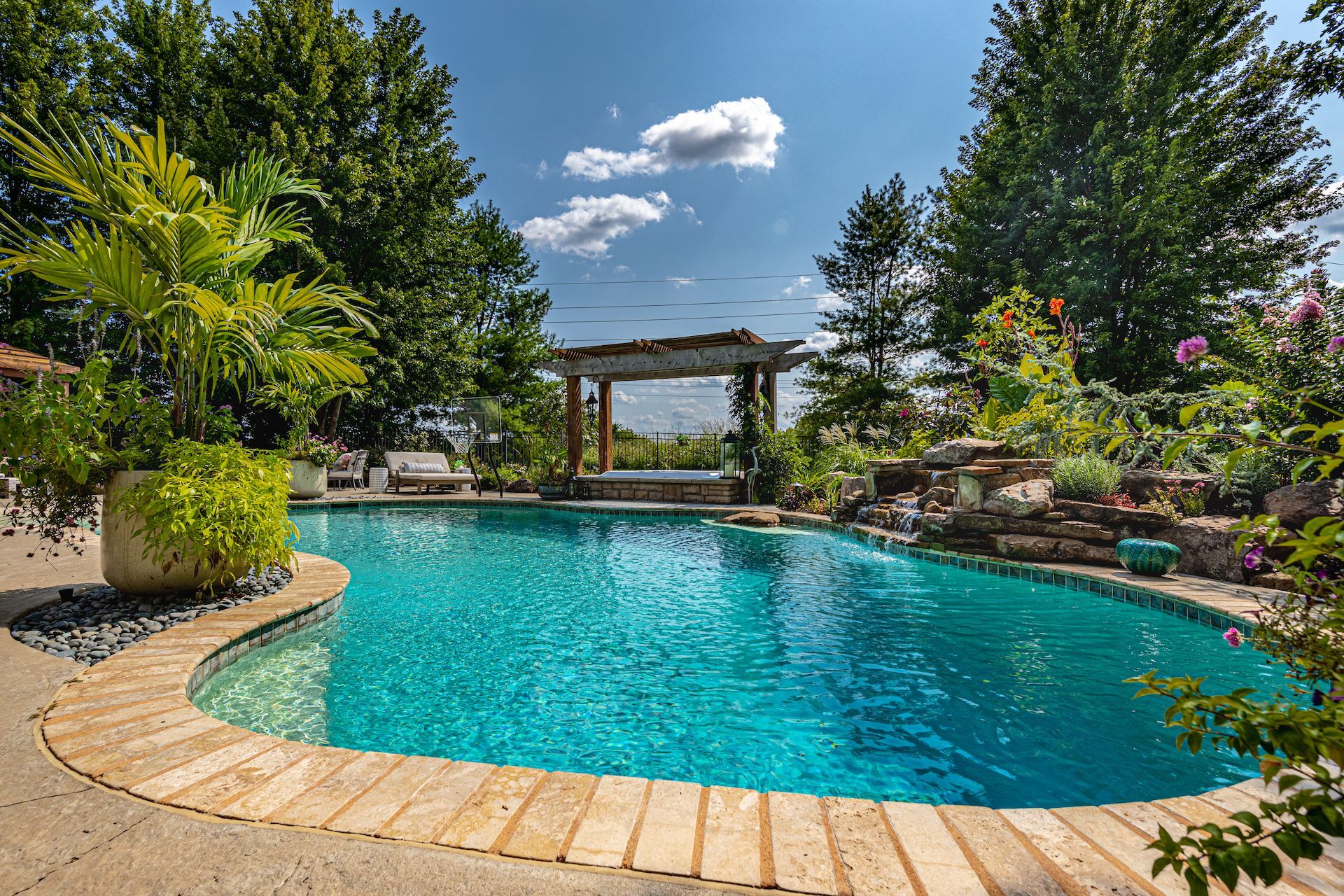 Landscaped backyard pool with turquoise water, stone edge, and pergola under a blue sky