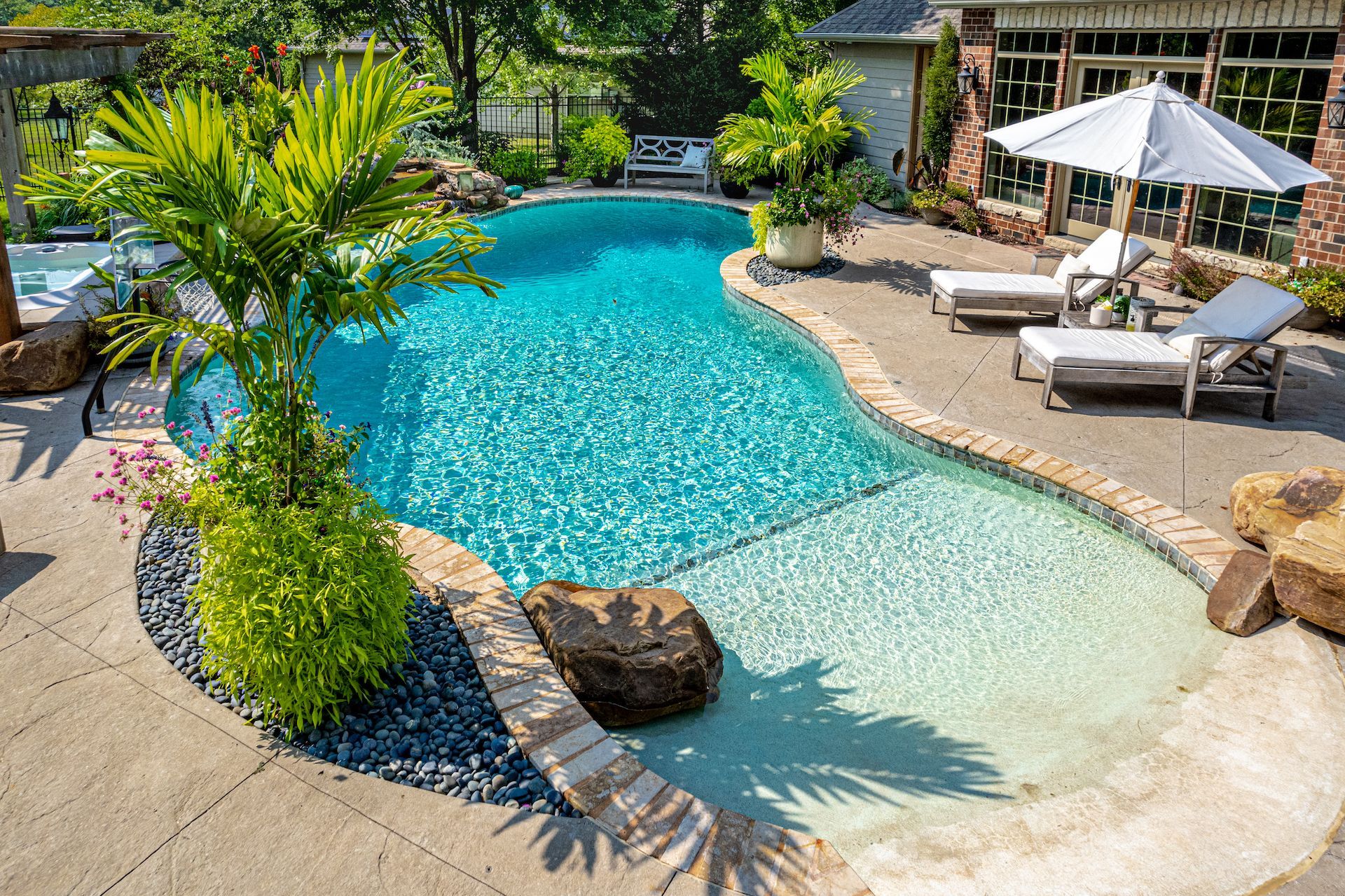 Backyard pool with turquoise water, stone patio, and white lounge chairs under an umbrella