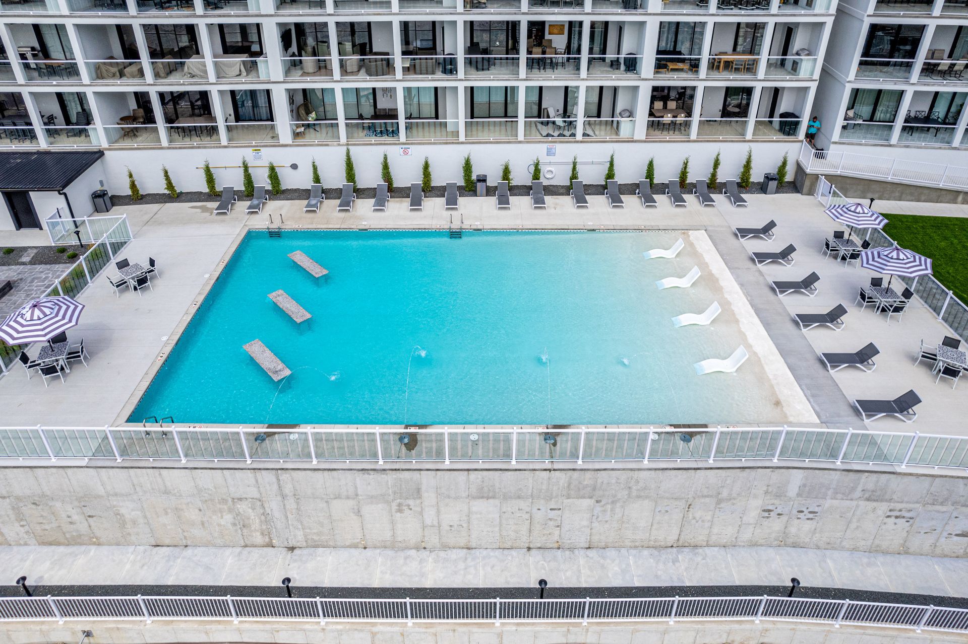 Modern hotel pool with turquoise water, lounge chairs, and a white multi-story building in the background