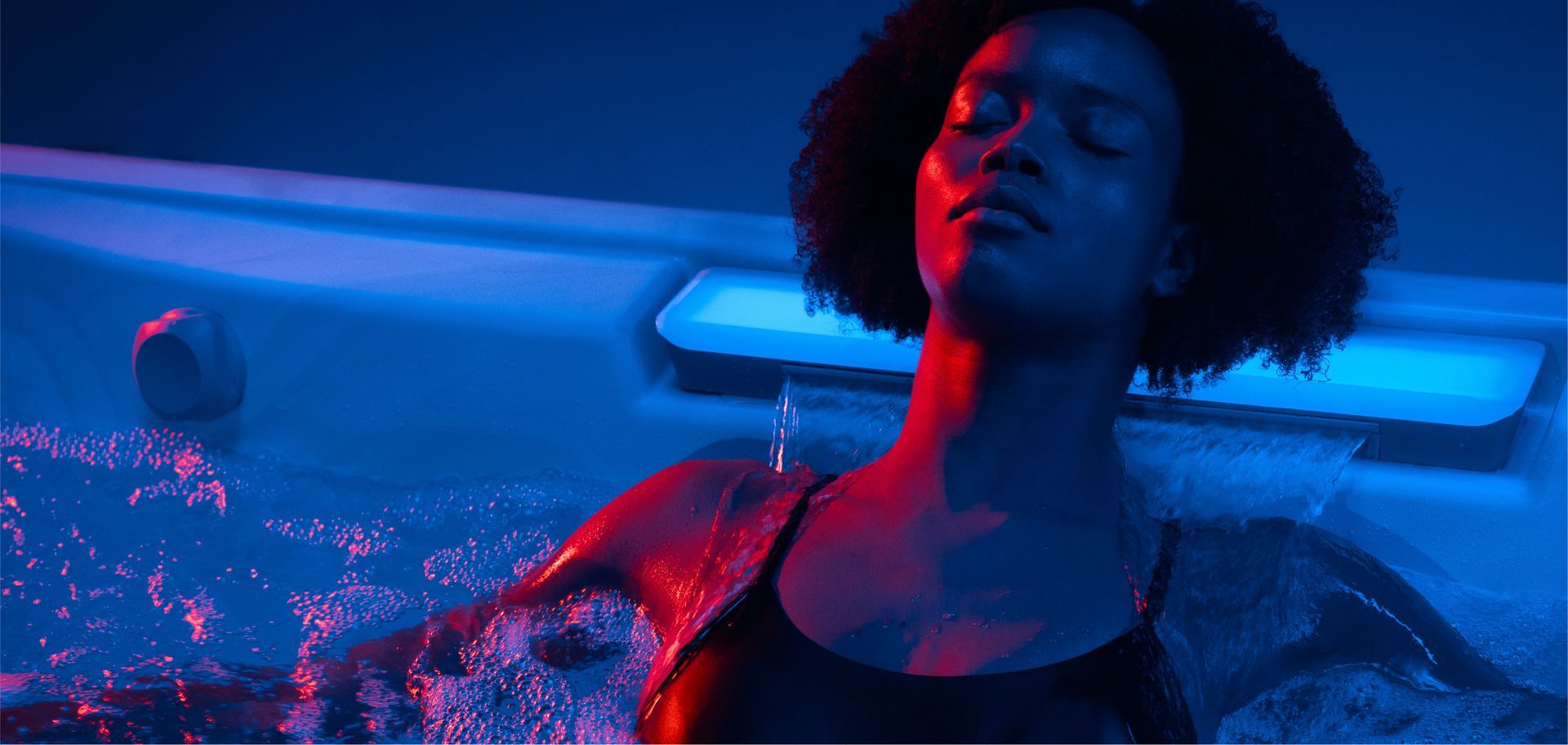 Woman floating in blue and pink neon-lit water, eyes closed and arms outstretched