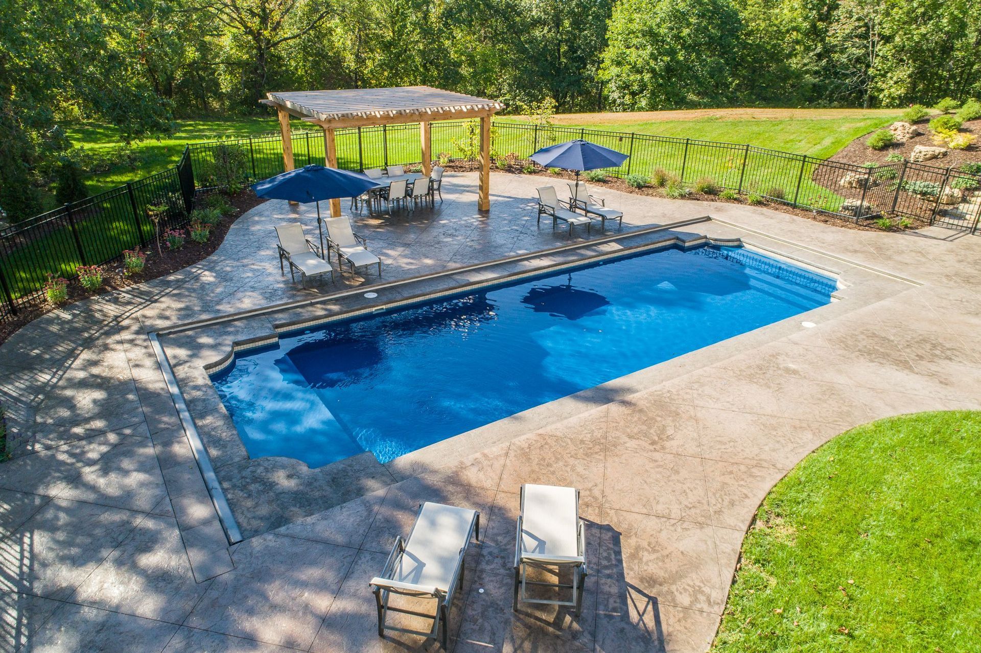 Backyard pool with blue water, lounge chairs, umbrellas, and a small gazebo surrounded by greenery